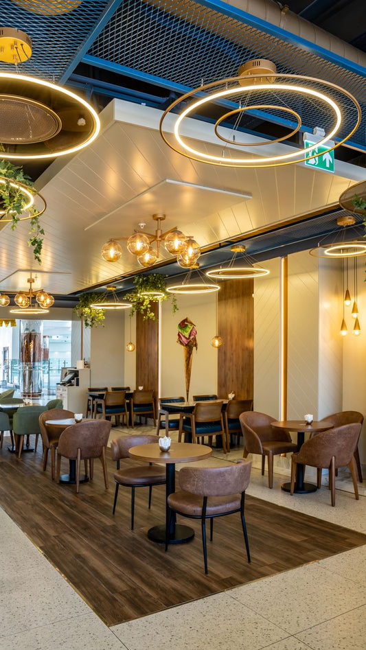 Modern brown faux leather café chairs with wooden tables and ring ceiling lights for a cozy, upscale coffee shop or casual dining experience.