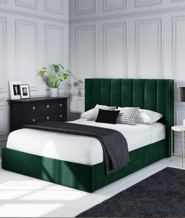 A modern green velvet upholstered bed with a tall, tufted headboard in a stylish bedroom with white panel walls and black decor accents.