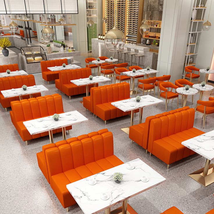 Modern restaurant interior with vibrant orange booth seating, marble-top tables, and gold-accented chairs in a stylish, well-lit space.