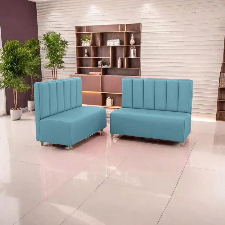 A modern blue faux leather restaurant booth sofa with vertical tufting and a high backrest, placed in a stylish interior with decorative shelves and plants.