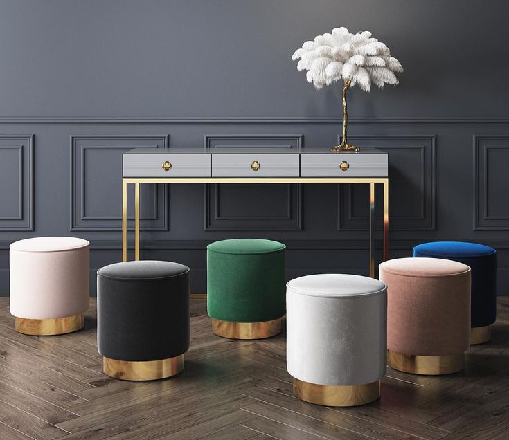 A stylish console table with gold accents, complemented by six velvet ottomans in different colors with gold bases, set against a dark paneled wall.
