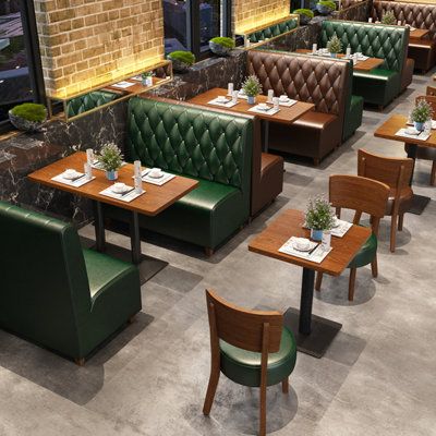 Modern cafe interior with green and brown diamond-stitched leather booth seating, wooden tables, and cushioned wooden chairs arranged neatly.