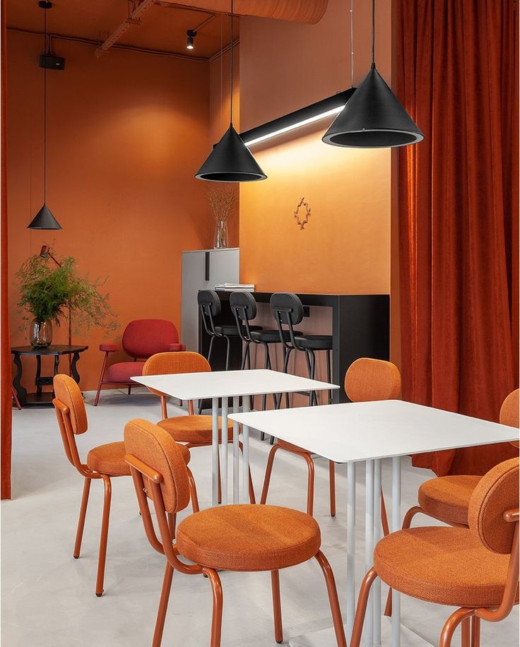 Modern café interior with burnt orange cushioned chairs, white square tables, and bold orange walls with black pendant lights