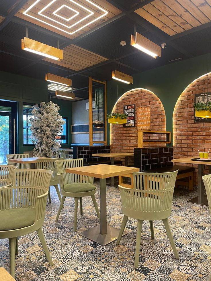 Café interior featuring muted green chairs, wooden square tables, patterned tiled flooring, brick arches, and modern hanging lights.