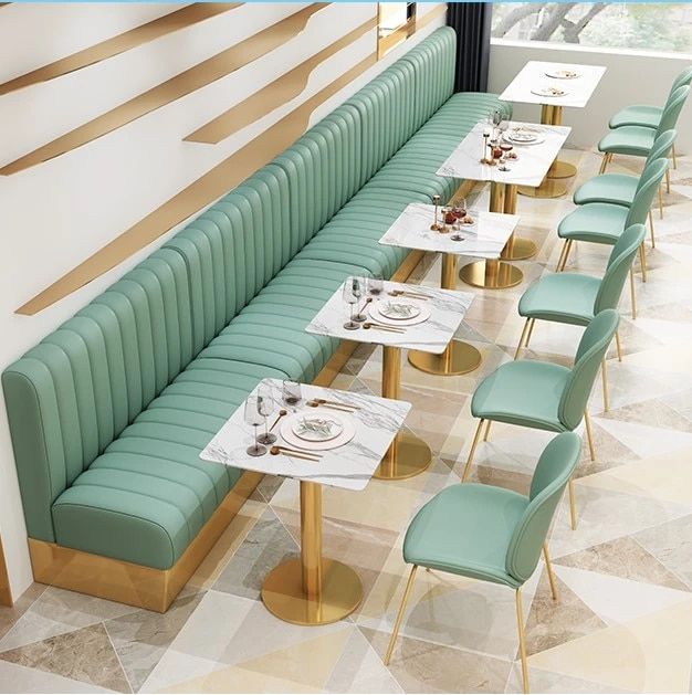 Luxury café interior featuring pastel green upholstered seating, marble top tables with gold bases, and stylish dining chairs.