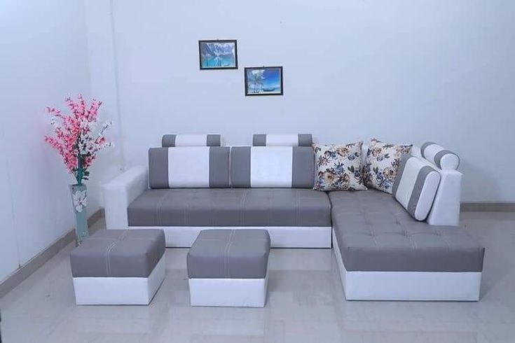 Minimalist grey and white L-shaped sectional sofa with tufted seating, two ottomans, and floral accent pillows, placed in a modern living room setting.