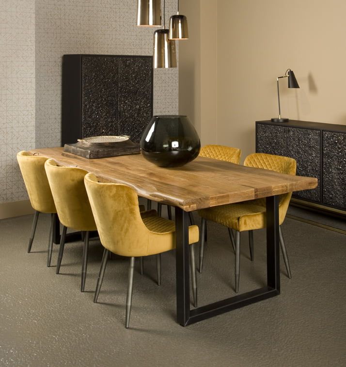 Rustic wooden dining table with a live-edge design, black metal legs, and mustard velvet chairs in a modern dining room with industrial-style décor and warm lighting.