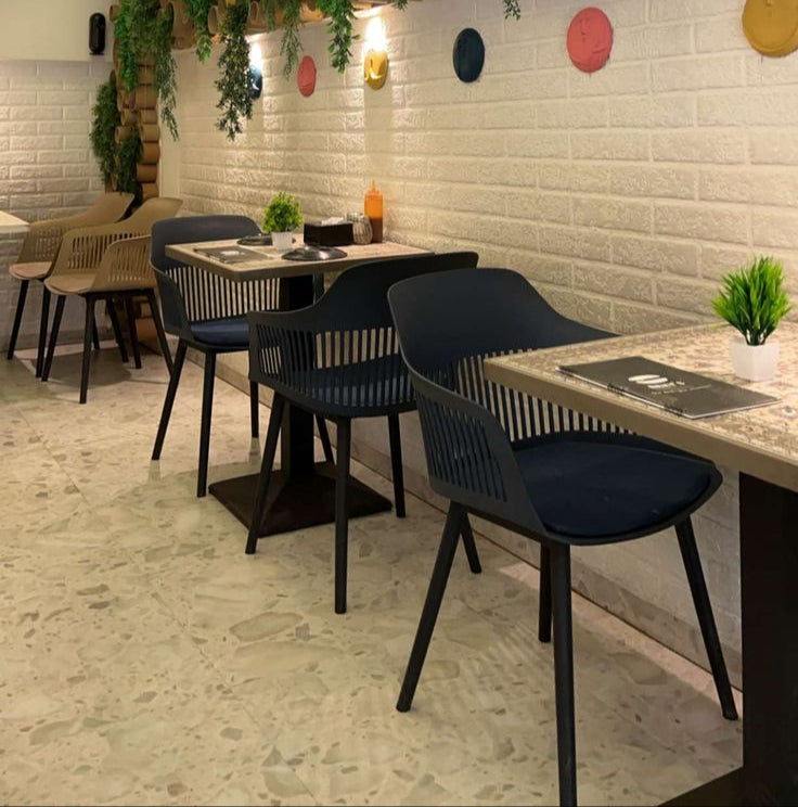 Modern café seating with black slatted chairs, rectangular tables, and wall-mounted greenery décor under stylish ceiling panels.