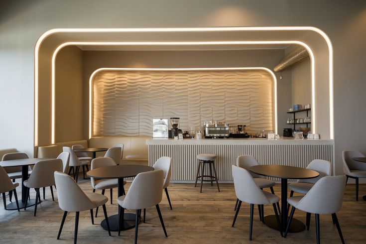 Modern café with beige chairs, round black tables, textured bar wall, and ambient LED lighting in a minimalist setting.