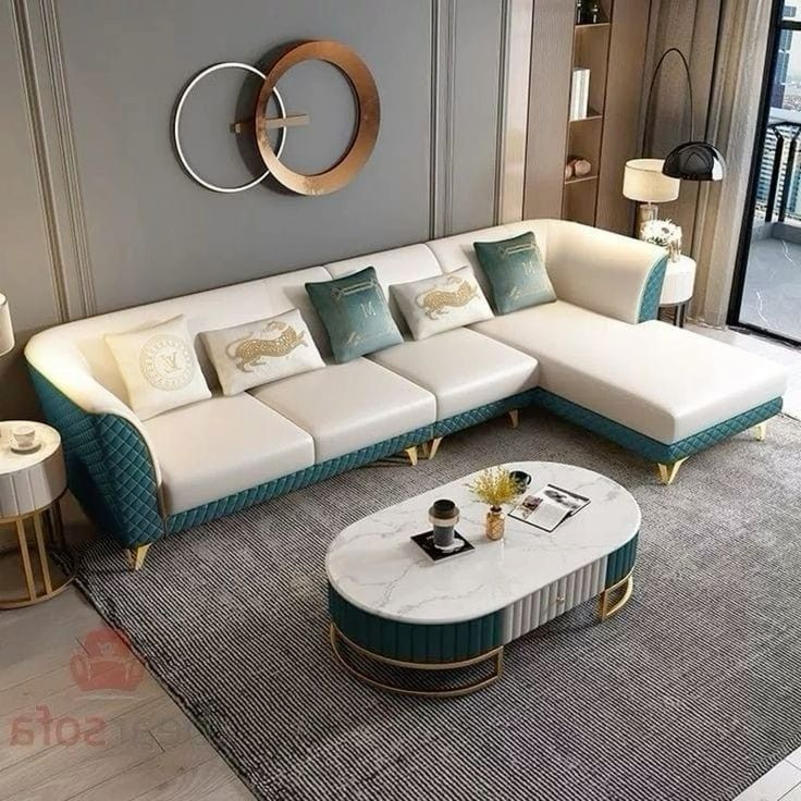 Modern L-shaped sectional sofa in white and teal with quilted armrests, gold legs, and plush cushions, placed in a stylish living room setting.