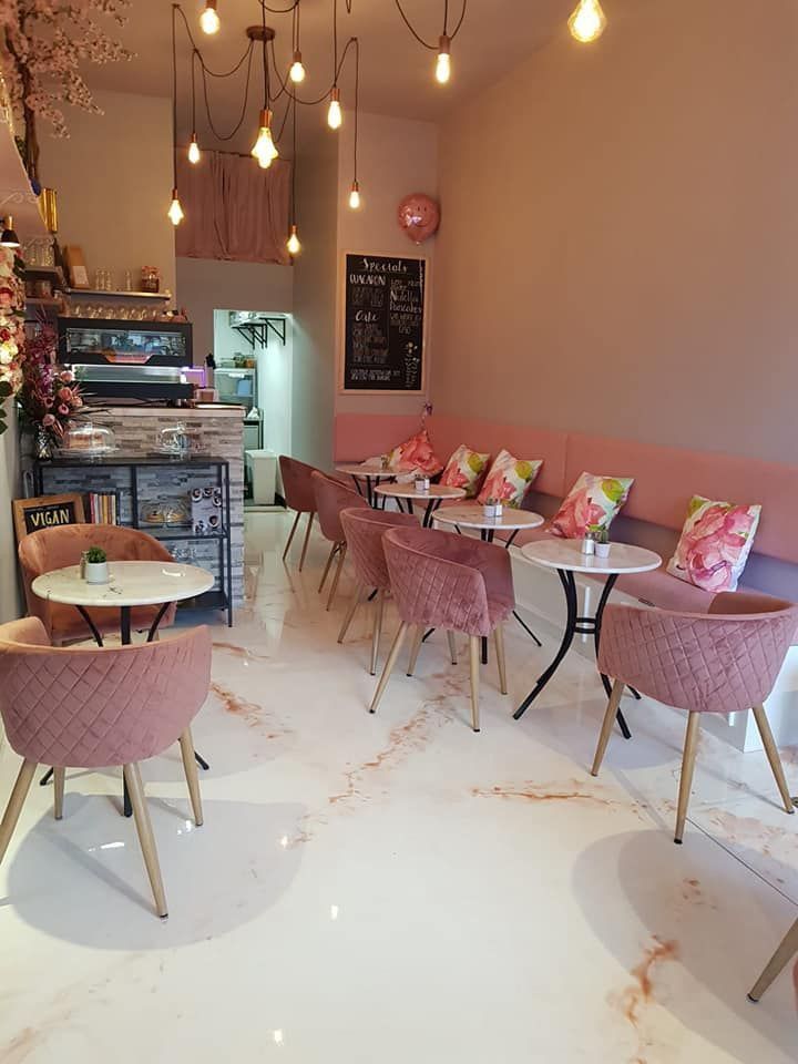 Cozy pink café interior with blush velvet chairs, marble-top round tables, floral cushions, and soft hanging lights.