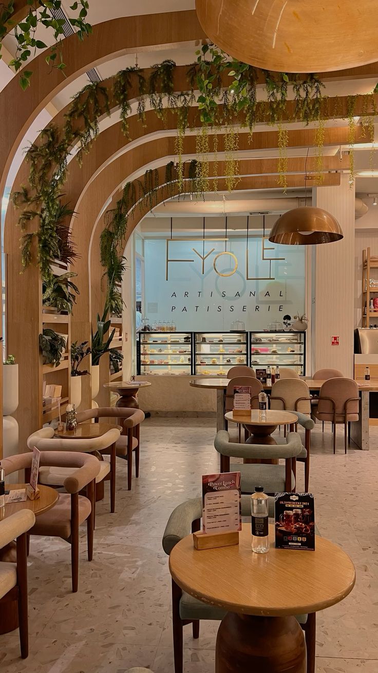 Modern café with curved wooden arches, green hanging plants, cozy round tables, and soft-toned chairs creating an earthy, elegant atmosphere.


