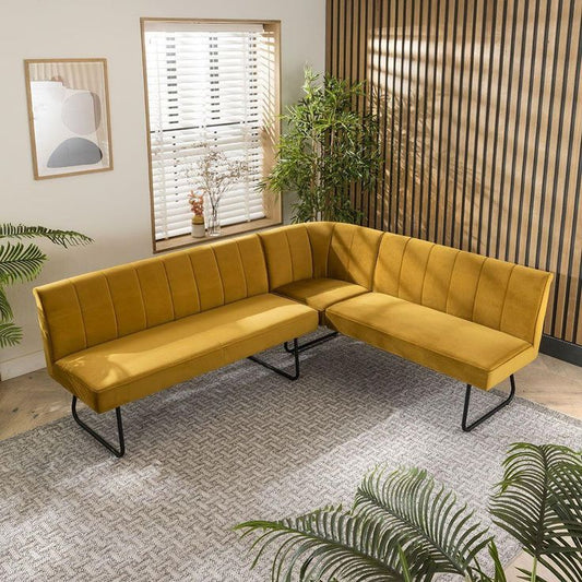 Modern dining set with a white marble table, mustard velvet chairs, and an L-shaped bench in a stylish dining room with wooden panel walls and indoor plants.