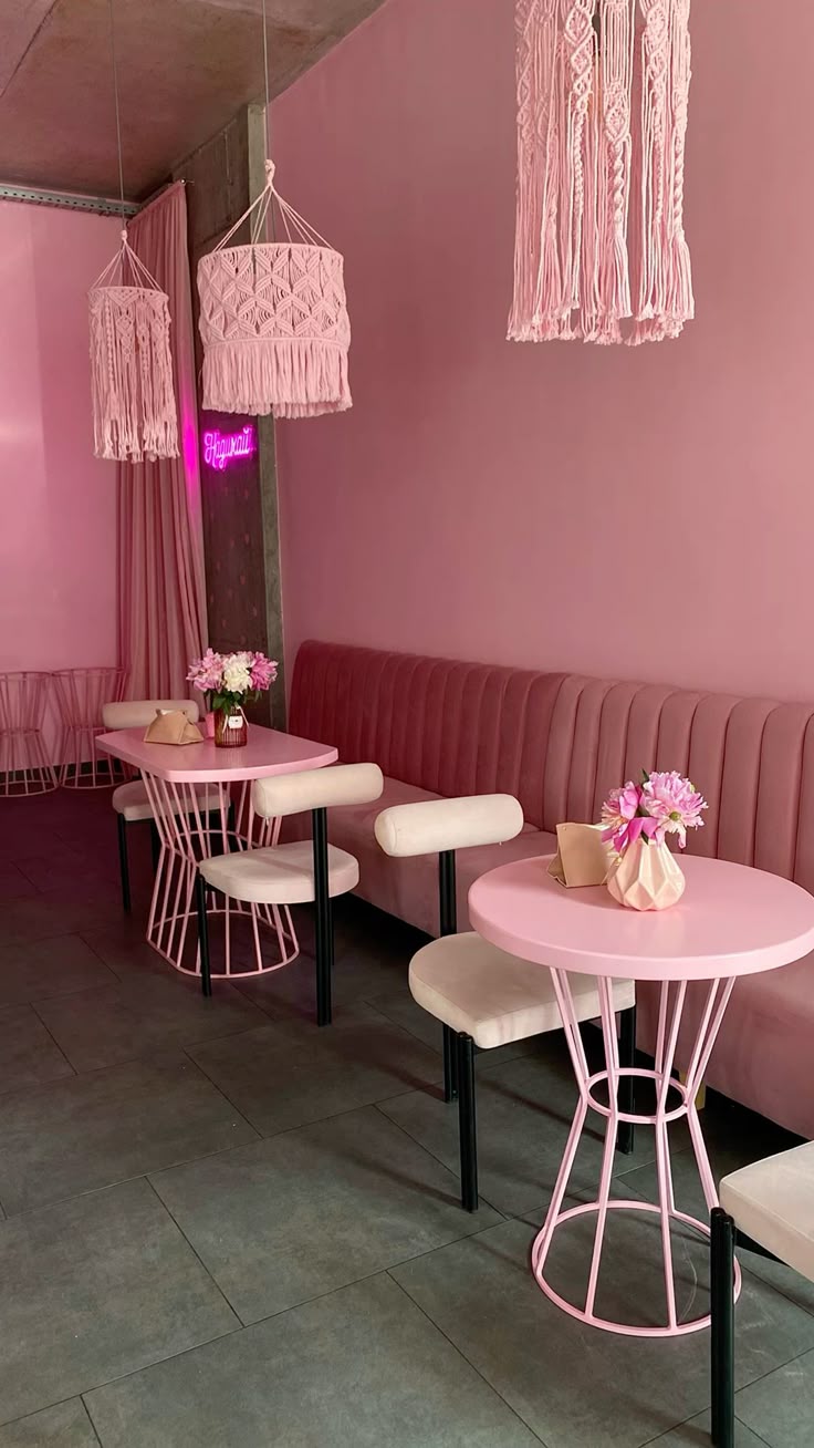 Pink café interior with round pastel tables, velvet bench seating, macramé pendant lights, and floral table decor