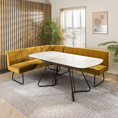 Modern dining set with a white marble table, mustard velvet chairs, and an L-shaped bench in a stylish dining room with wooden panel walls and indoor plants.